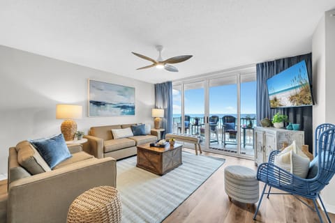 Unwind in your bright, coastal living room with ocean views framing the balcony. Sink into plush seating, enjoy the ceiling fan's breeze, and catch your favorite shows on the flat-screen TV.