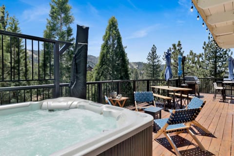 Outdoor deck with a jacuzzi, BBQ grill, dining table, and comfortable seating, offering beautiful mountain and pine tree views in a peaceful setting.