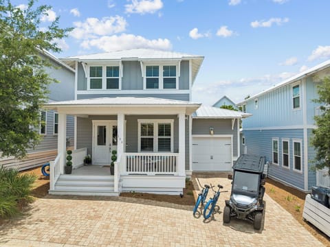 Charming coastal cottage with covered front porch and golf cart parking, nestled in a peaceful neighborhood setting.