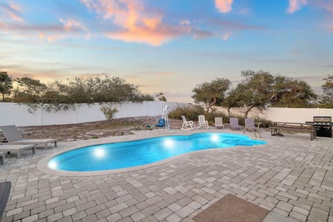 Pool area with evening sky colors in the background, surrounded by paved decking and lounge furniture.