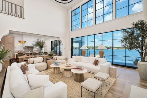 Sink into plush white sofas as natural light floods your waterfront living space through floor-to-ceiling windows.