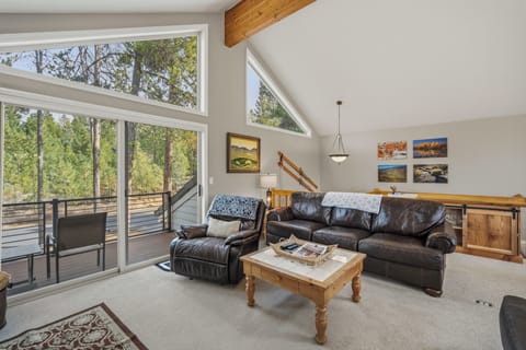 Unwind in your bright living room with forest views through floor-to-ceiling windows, comfortable leather seating, and peaceful tree-lined balcony.