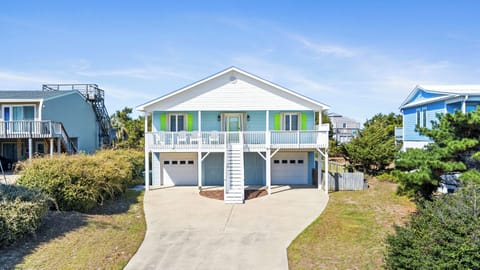 Charming coastal home with bright green shutters and spacious front porch, surrounded by mature landscaping in a peaceful beach community.