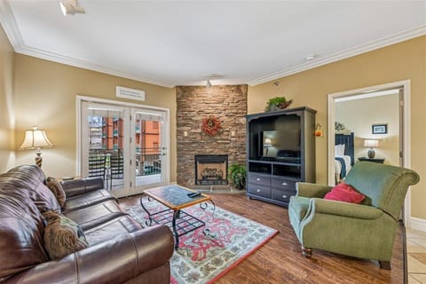 Unwind in your cozy living room with a stone fireplace, plush seating, and peaceful balcony access for relaxing evenings.