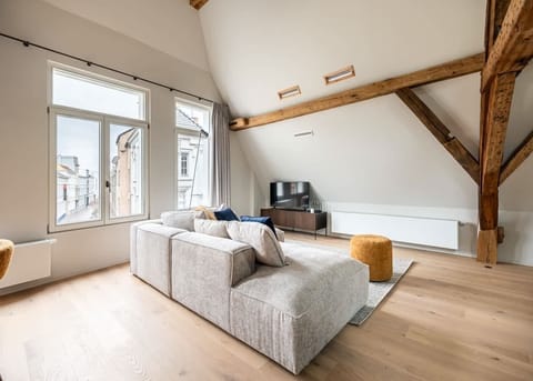 Modern living room with exposed wooden beams and large windows overlooking the street.