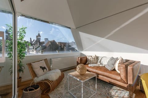 sunlit living area with a leather sofa and city views through a large angled window