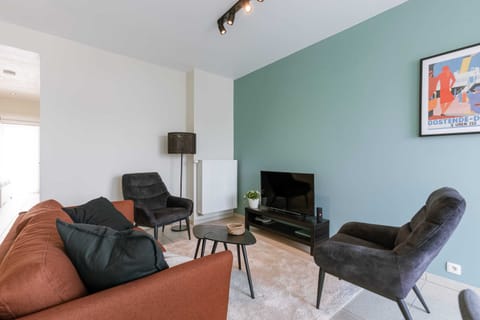 Cozy living room with a rust-colored sofa, black armchairs, and a modern entertainment setup against a muted green accent wall.