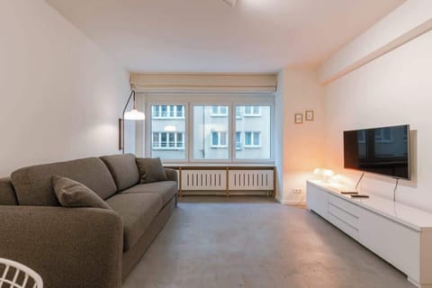 A bright, open-concept room designed for both relaxation and rest, featuring a large flat-screen TV and a comfortable sofa.