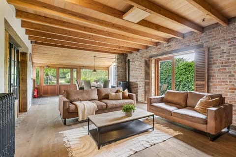 Rustic living room with exposed brick walls, wooden beams, and leather sofas overlooking a garden.