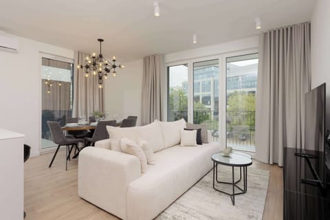 A bright living room with a white sofa, a small round coffee table, and large windows letting in natural light.