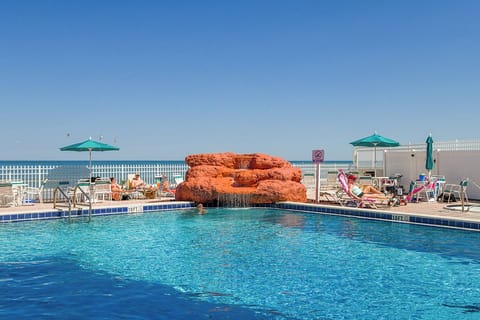 Sparkling pool with decorative rock waterfall creates your perfect poolside retreat under the bright blue sky.
