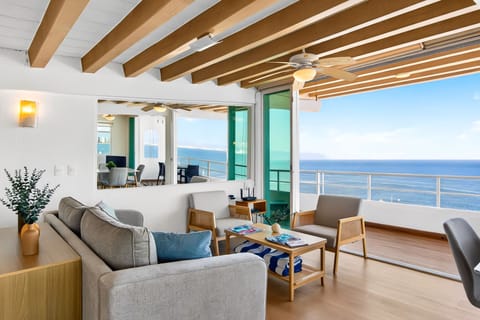 Sunlit living area with comfortable sofas and wooden beams, opening up completely to a private ocean-view balcony.