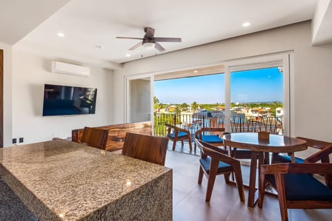 Relax in a sunlit open-concept layout featuring a polished granite counter, warm wood dining set, and wide sliding doors opening to the balcony.