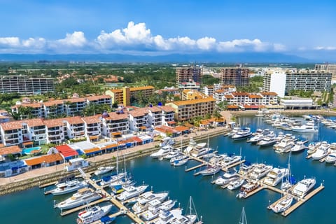 A stunning, high-angle aerial view capturing a vibrant marina filled with luxury yachts and boats, bordered by a beautiful coastal resort complex.
