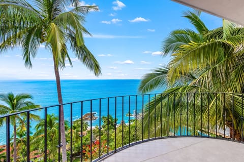 Breathtaking view from a private curved balcony overlooking the vibrant blue sea and tropical palm trees.
