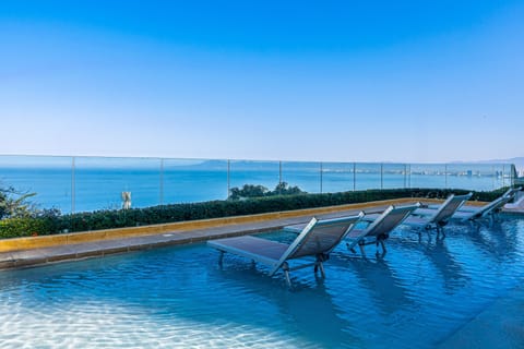 Submerged lounge chairs on a shallow pool ledge with panoramic ocean views.