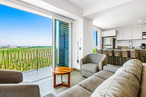 Relax in this bright, open-concept living space that flows effortlessly past a comfortable sofa setup into a sleek modern kitchen with balcony access.