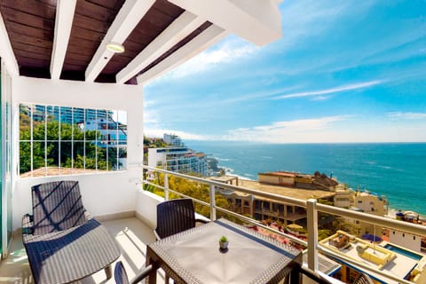 Covered outdoor balcony featuring a dining table set, dark wicker chairs, and a stunning panoramic view of the coastline and ocean.