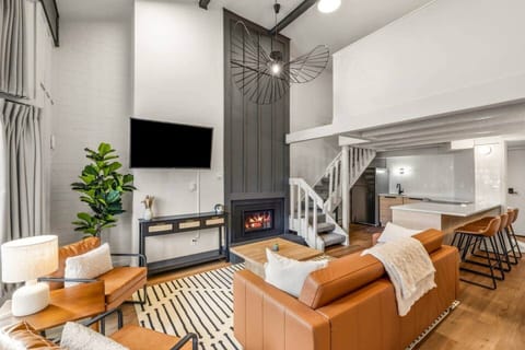 Light-filled living space with soaring ceilings, curated mid-century furnishings, and warm leather seating centered around a modern fireplace. Statement lighting and refined textures create an inviting, elevated retreat after a day on the slopes.