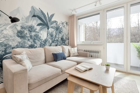 A cozy lounge space with a plush sofa, a wooden coffee table, and large windows that brighten the room. The soft color palette and subtle decor create a relaxing environment.