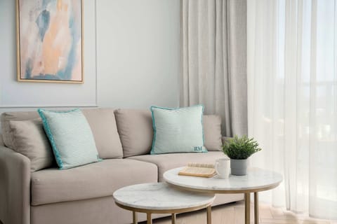 A cozy living area features a plush sofa adorned with light blue pillows and two circular coffee tables. A small potted plant and an abstract art piece add character to the minimalist space. 