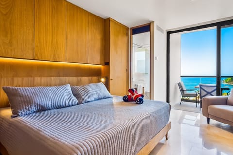 Rest comfortably in a bright bedroom featuring warm wood finishes, modern furnishings, and direct access to ocean-view outdoor spaces.