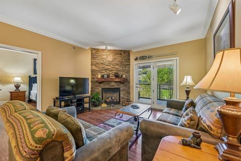 Relax in your cozy living room with stone fireplace, plush seating, and garden views through French doors.