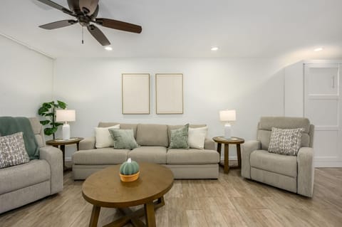 Light wood floors ground the living room with beige sofas, green accent pillows, and two round wood side tables.