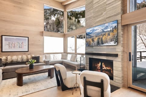 Bright and inviting living room with floor-to-ceiling views of Aspen Mountain. Enjoy a wood-burning fireplace and interiors designed by local Aspen award-winning interior designer.