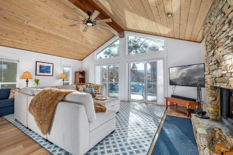 Living room with sectional sofa, TV, fireplace, ceiling fan, sliding doors, deck, canal view, and ottoman.