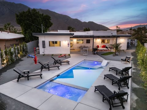 Twilight backyard with lit pool, spa, and mountain backdrop