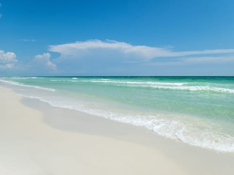 Pristine white sand beach with crystal-clear turquoise waters and gentle waves under a brilliant blue sky.