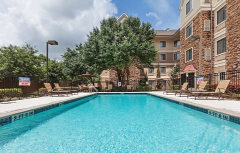 The inviting pool area features clear water surrounded by comfortable lounge chairs and trees for shade, perfect for relaxation.