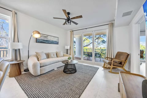 Modern living room with a curved sofa and balcony access overlooking trees.