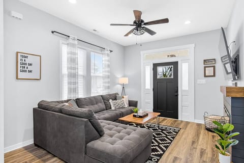 A bright, stylish lounge with a plush sectional, electric fireplace, and large Roku TV—your cozy spot to unwind steps from the kitchen and first bedroom.