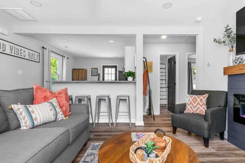 Well‑lit and centrally located between the kitchen and bathroom, this inviting space is your cozy retreat. with a plush sofa, two cozy armchairs, and a large wall‑mounted flat‑screen TV—anchored by a modern remote‑controlled electric fireplace.