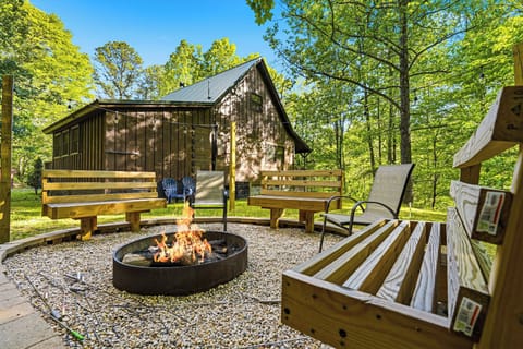 Rustic cabin nestled among towering trees with outdoor fire pit, wooden benches, and peaceful forest setting.