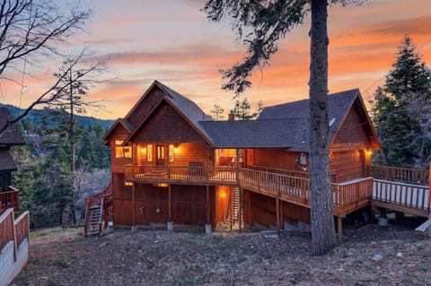 Warm, glowing mountain cabin surrounded by towering pines and sunset skies.