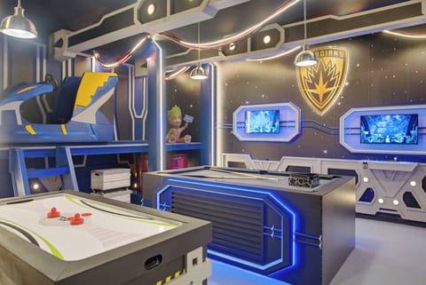 Experience a lively game room filled with excitement, featuring sleek blue LED lighting and a modern design. Enjoy friendly competition on the air hockey table and video game consoles, all surrounded by fun decor.