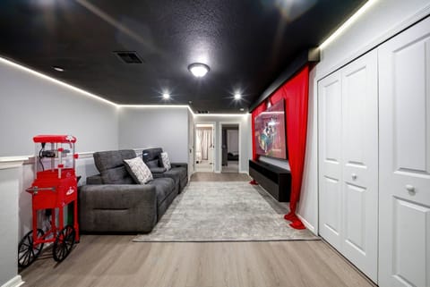 Experience a cozy entertainment area with a plush gray sectional couch perfect for relaxing. Dramatic red curtains frame a large screen, and soft lighting adds a modern vibe, making it ideal for movie nights or game days.