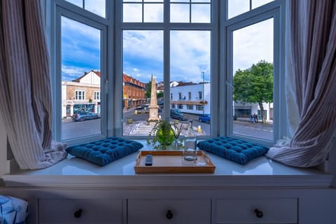 - Bay window seat with cushions tray water and plant decor setup   - Natural light brightens this relaxing space with city views   - Cozy corner for reading enjoying coffee or unwinding calmly 