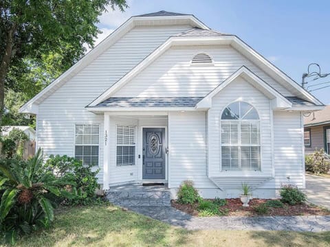 Welcome to your Pensacola retreat! This bright, coastal-style home features crisp white siding, arched windows, and a shaded entryway surrounded by lush greenery. A warm first impression awaits just beyond the door.