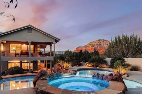 A stunning desert property featuring illuminated pool and red rock mountain backdrop at sunset.