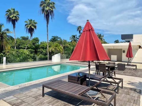 Shared pool deck w/ loungers & bold red umbrellas surrounded by lush greenery