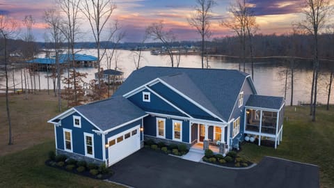 Exterior - A sweeping twilight aerial shows the full front elevation, garage, screened porch, and lit boathouse behind.