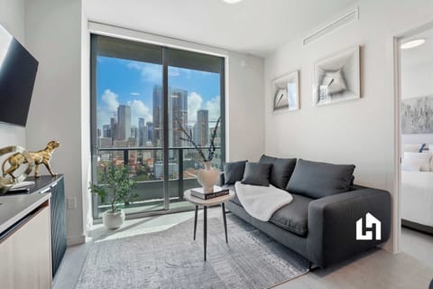 Sunlit living space with modern furnishings and floor-to-ceiling windows overlooking the downtown skyline.
