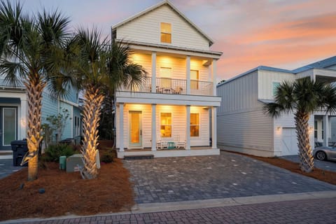 Charming two‑story beach house with double porches, light‑blue accents, and palm‑lined curb appeal.
