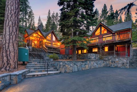 Grand mountain lodge glowing with warm light, surrounded by towering pines and rustic stone pathways.