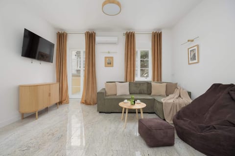 A spacious living room with a gray sofa, a wooden TV stand, and a wall-mounted TV. Light-colored walls and a glossy floor give the interior a modern feel.