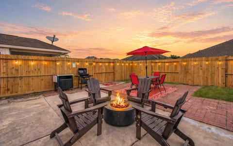 Backyard hangout goals—fire pit lounge, glowing string lights, BBQ grill, and a vibrant dining setup under the umbrella for perfect evening vibes.